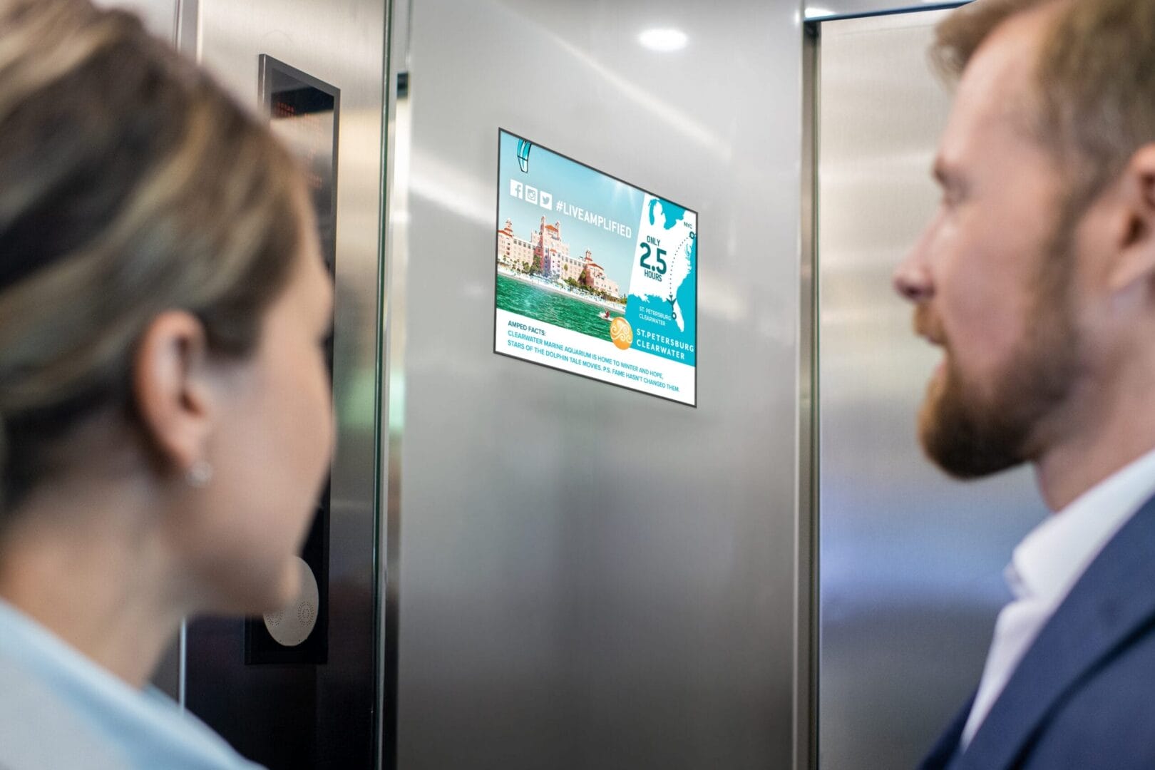 Two people looking at an advertisement on an elevator panel.