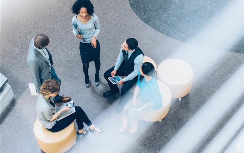 Group of five professionals having a discussion while sitting on round chairs in a modern office setting.