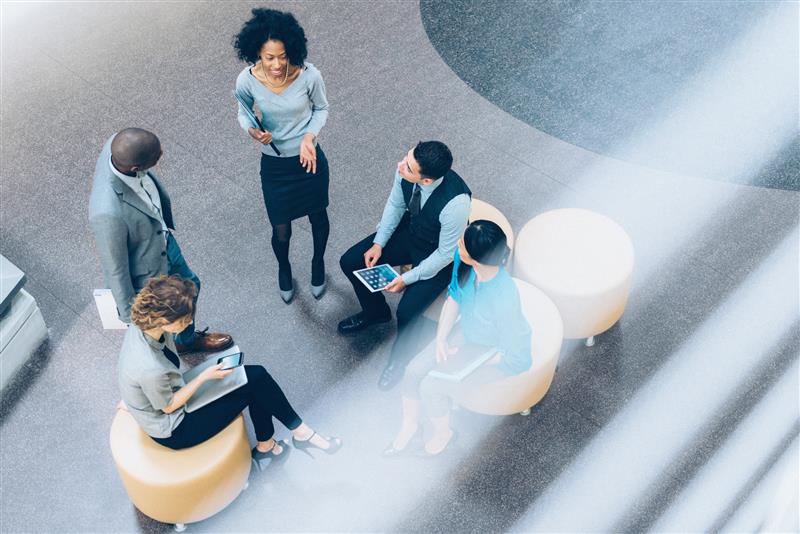 Group of five professionals having a discussion while sitting on round chairs in a modern office setting.