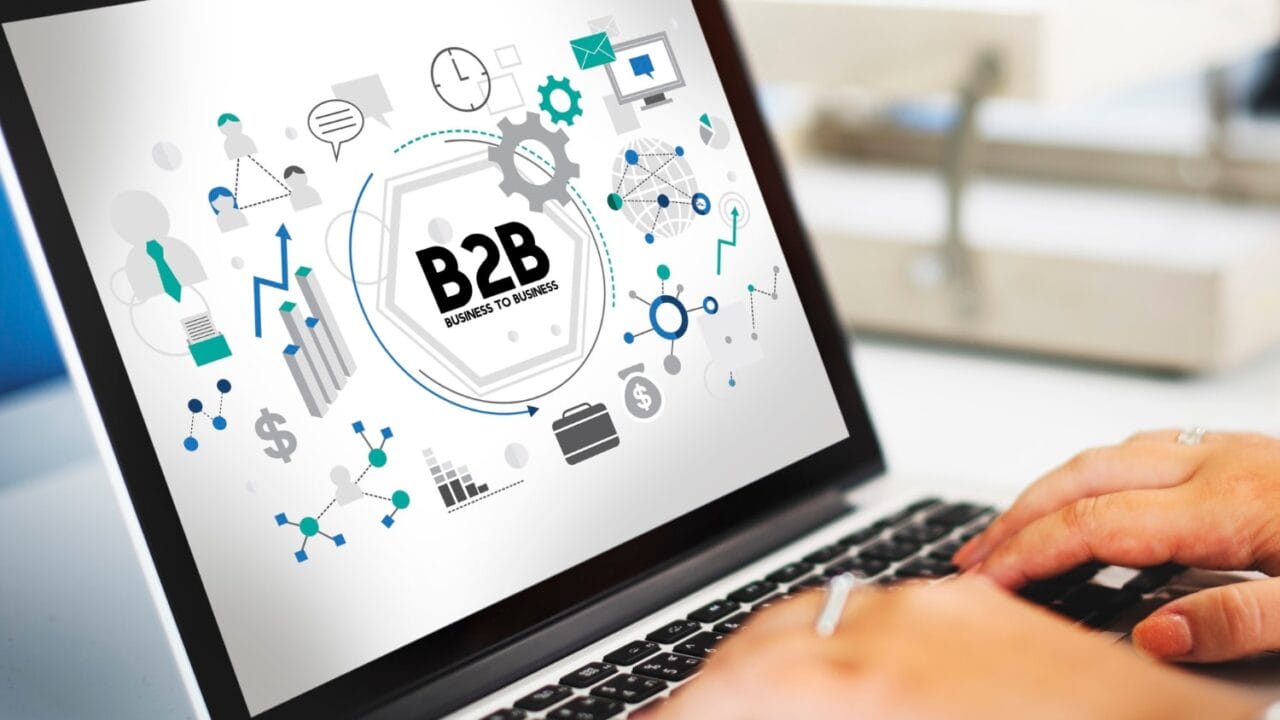 Laptop displaying B2B business graphics with charts and icons as hands type on keyboard.