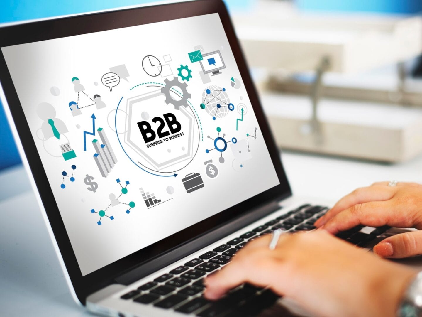 Laptop displaying B2B business graphics with charts and icons as hands type on keyboard.