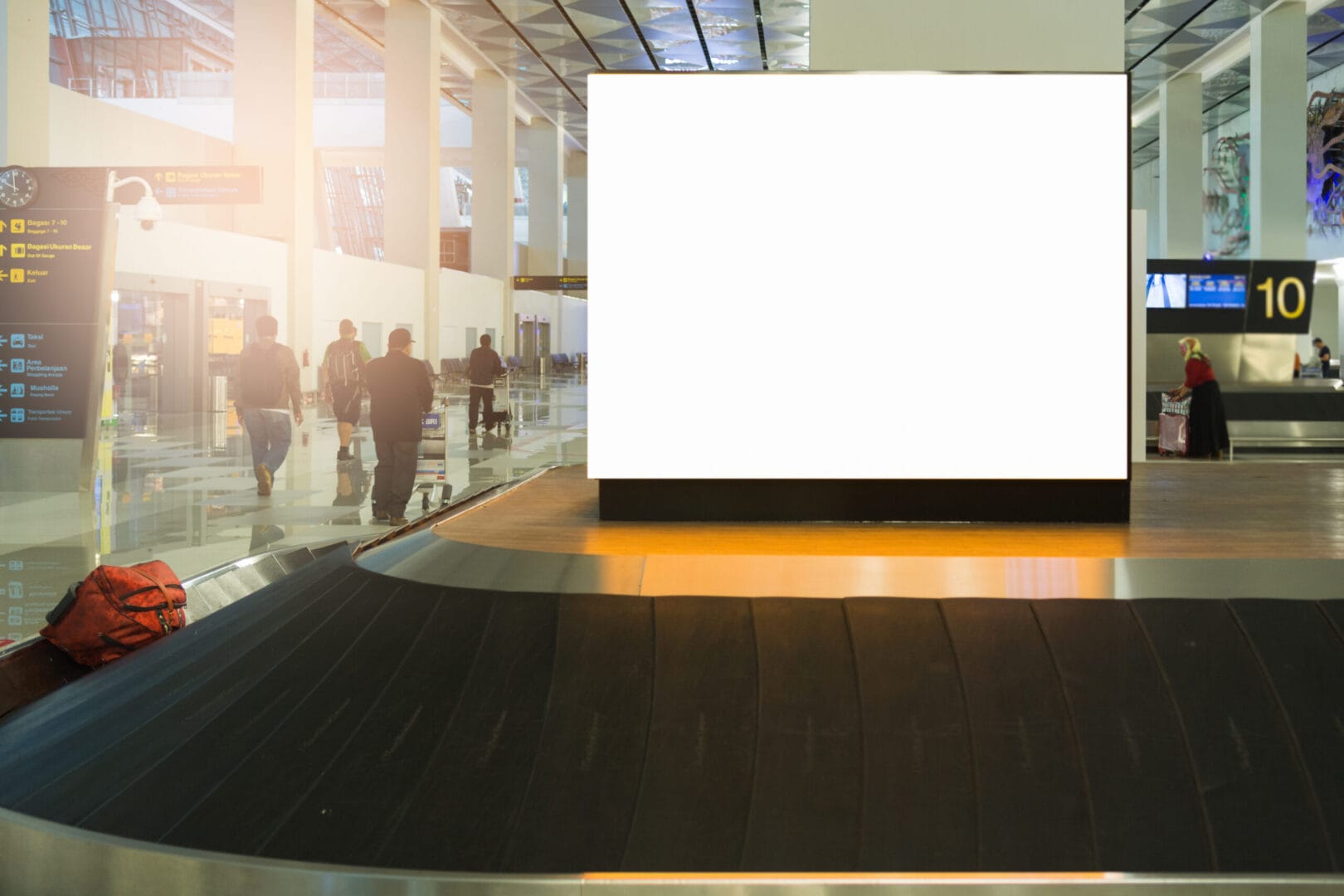 Blank billboard at airport baggage claim with people in the background.