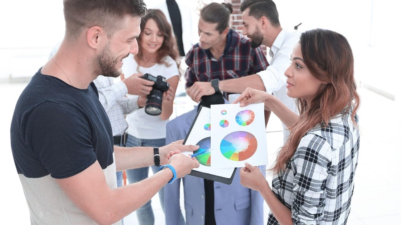 Group of young professionals discussing color schemes and photography in a bright office space.
