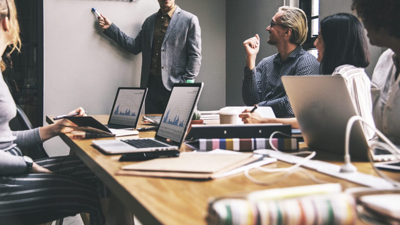 Employees in a meeting room discussing strategies, surrounded by laptops and graphs on the table.