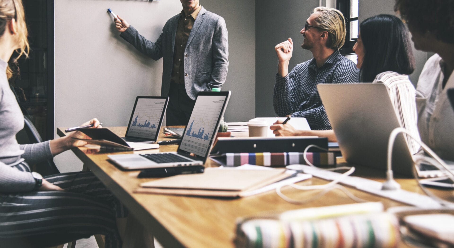 Employees in a meeting room discussing strategies, surrounded by laptops and graphs on the table.