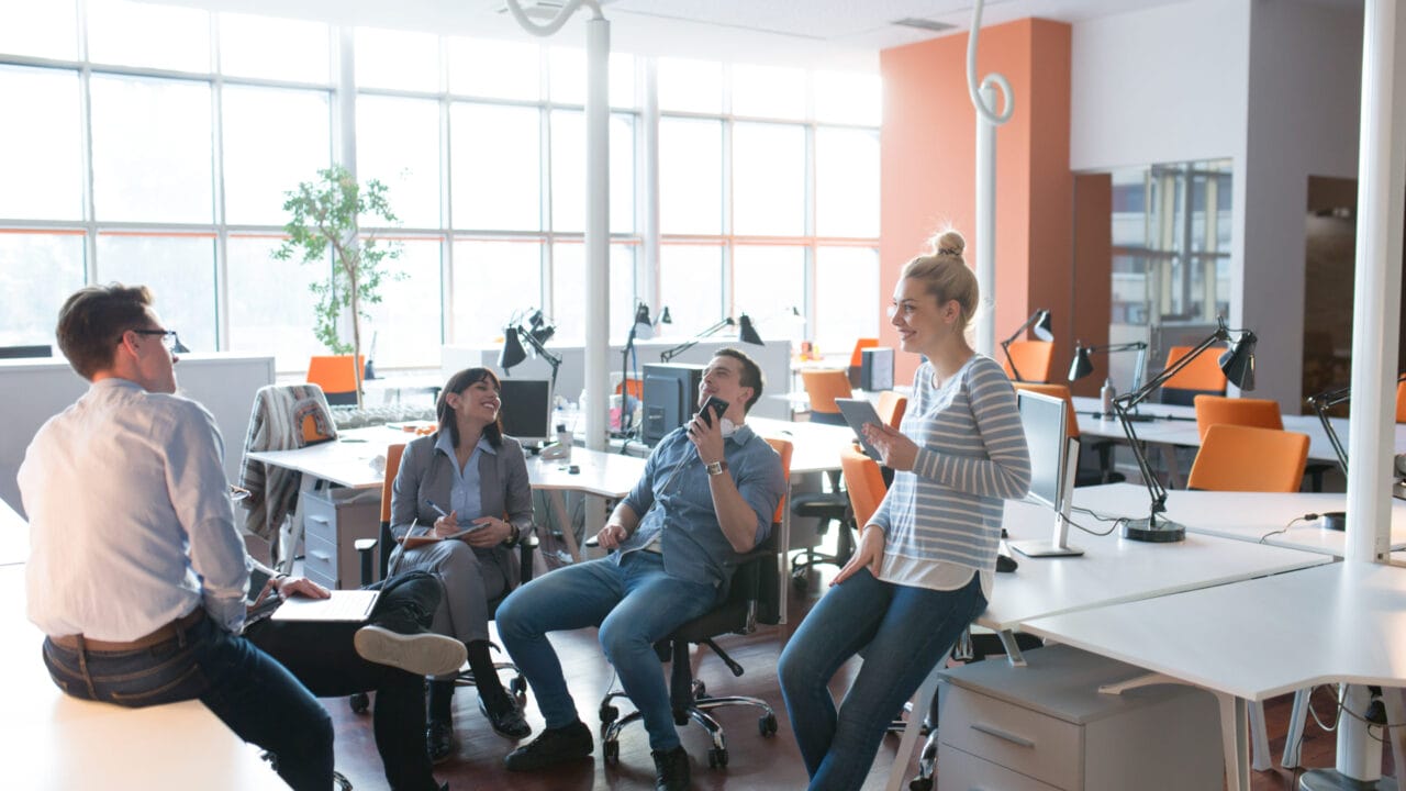 People having a casual meeting in a bright modern office space with desks and computers.