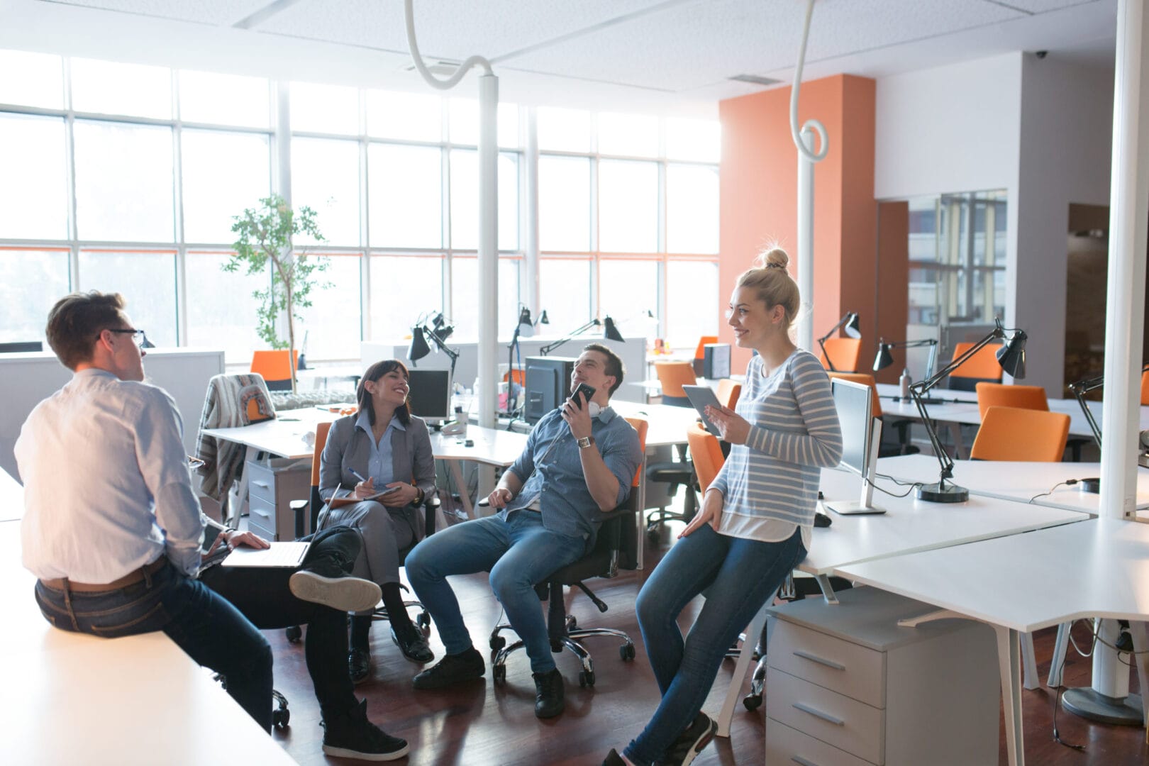 People having a casual meeting in a bright modern office space with desks and computers.