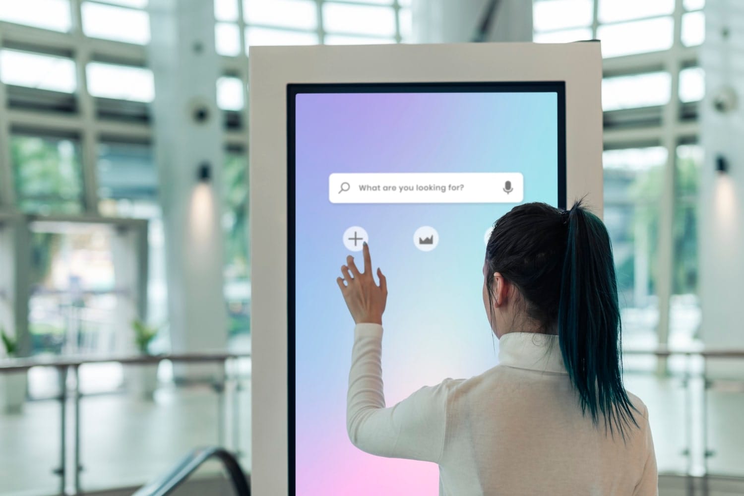 Person using a touchscreen kiosk with search bar in a modern building lobby.