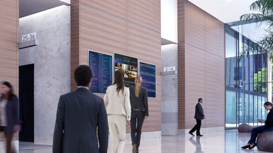 People walking through a modern office lobby with digital screens and natural lighting.