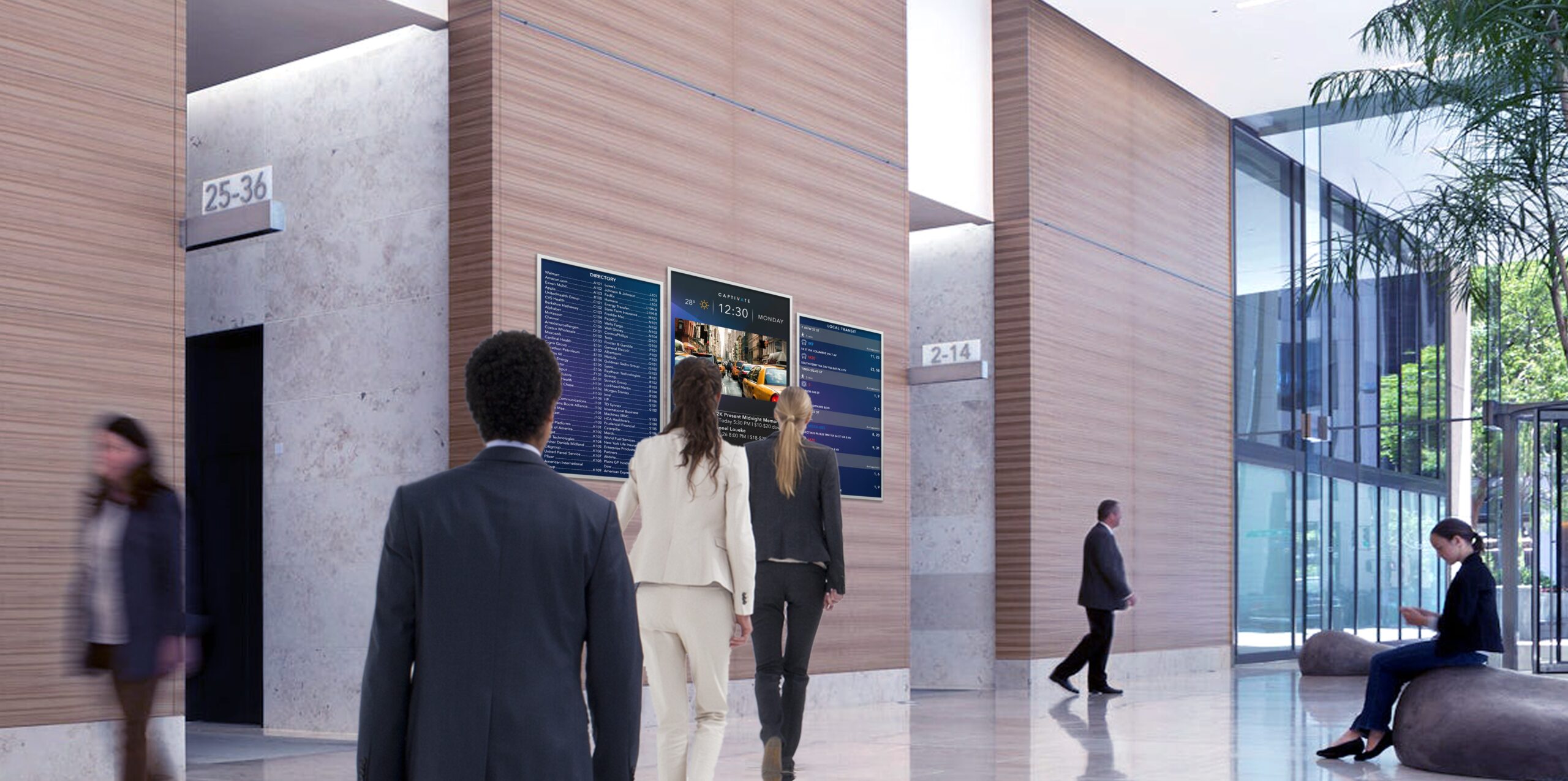 People walking through a modern office lobby with digital screens and natural lighting.