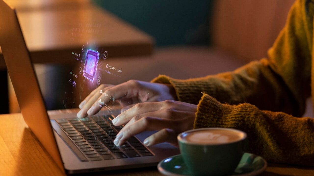 Person typing on laptop with digital holograms above keyboard, cup of coffee on table in warm ambient light.