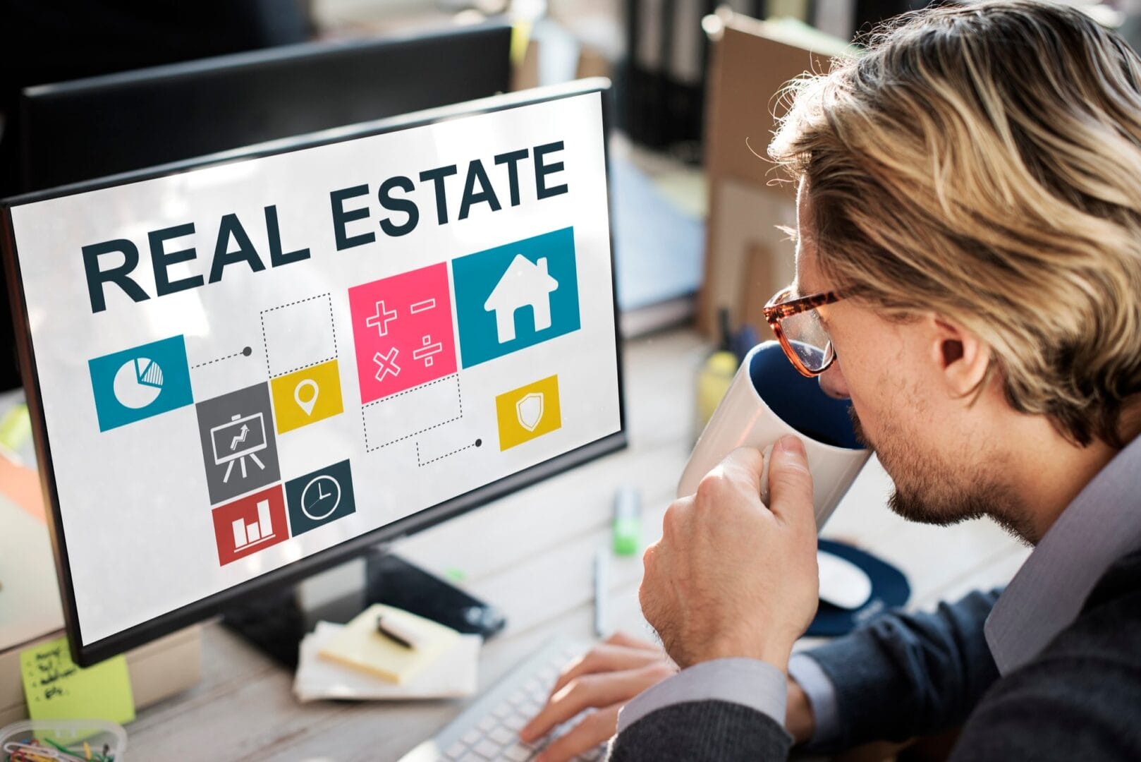 Person drinking coffee while analyzing real estate information on a computer screen with charts and icons.