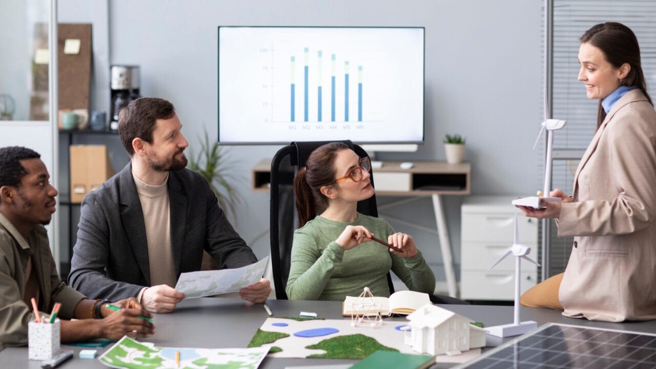 Team discussing renewable energy plans in modern office setting with charts and models on the table.