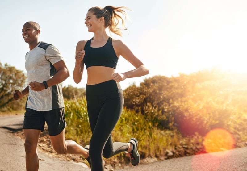 Two people jogging outside on a sunny day with greenery in the background