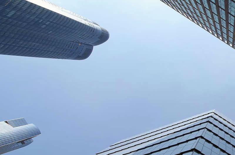 Upward view of modern skyscrapers against a clear blue sky. Symmetrical architecture and glass facades reflecting sunlight.