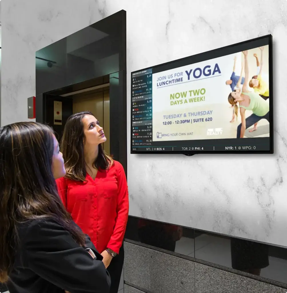 People looking at a digital sign advertising lunchtime yoga classes held twice a week in an office building lobby.