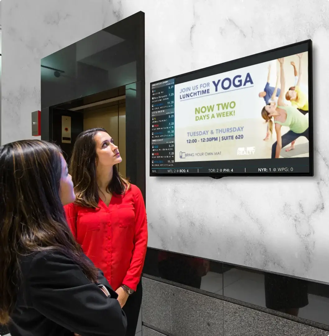 People looking at a digital sign advertising lunchtime yoga classes held twice a week in an office building lobby.