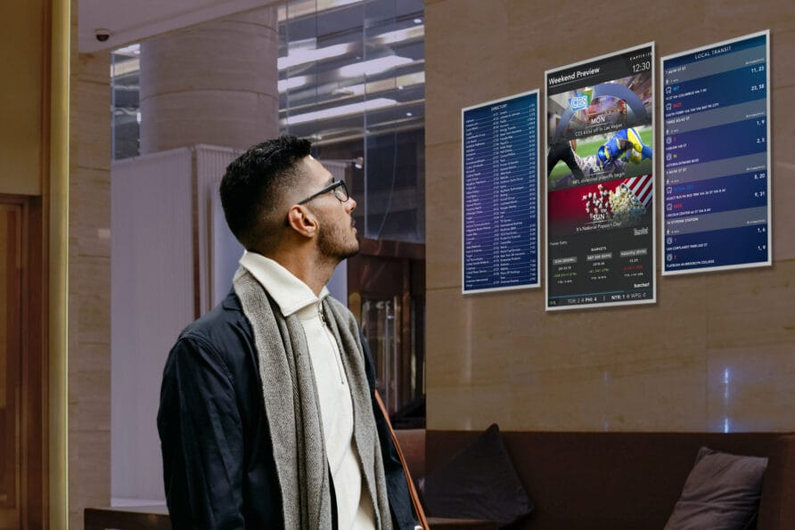 Man looking at sports betting odds on digital screens in a modern lobby setting.