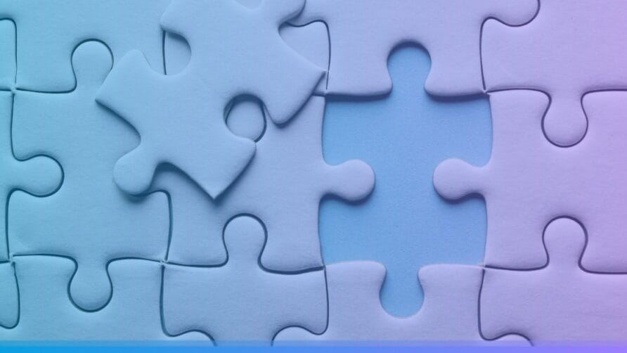 Puzzle pieces in various shades of blue and purple, with one piece missing and another resting on top of the puzzle.