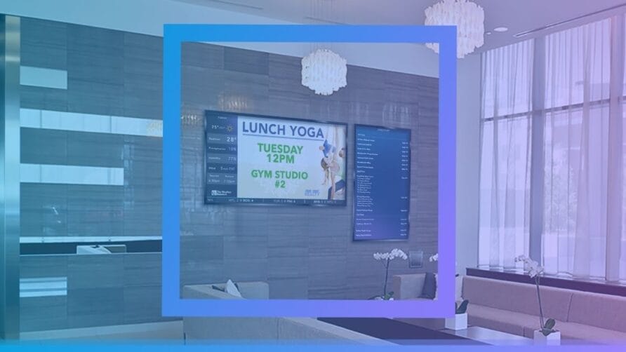 Digital sign in modern lobby displaying "Lunch Yoga Tuesday 12PM Gym Studio #2" with seating and decor in the background.