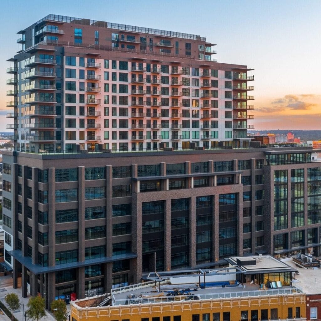 Modern multi-story building with glass windows, set against a vibrant sunset sky in an urban landscape.