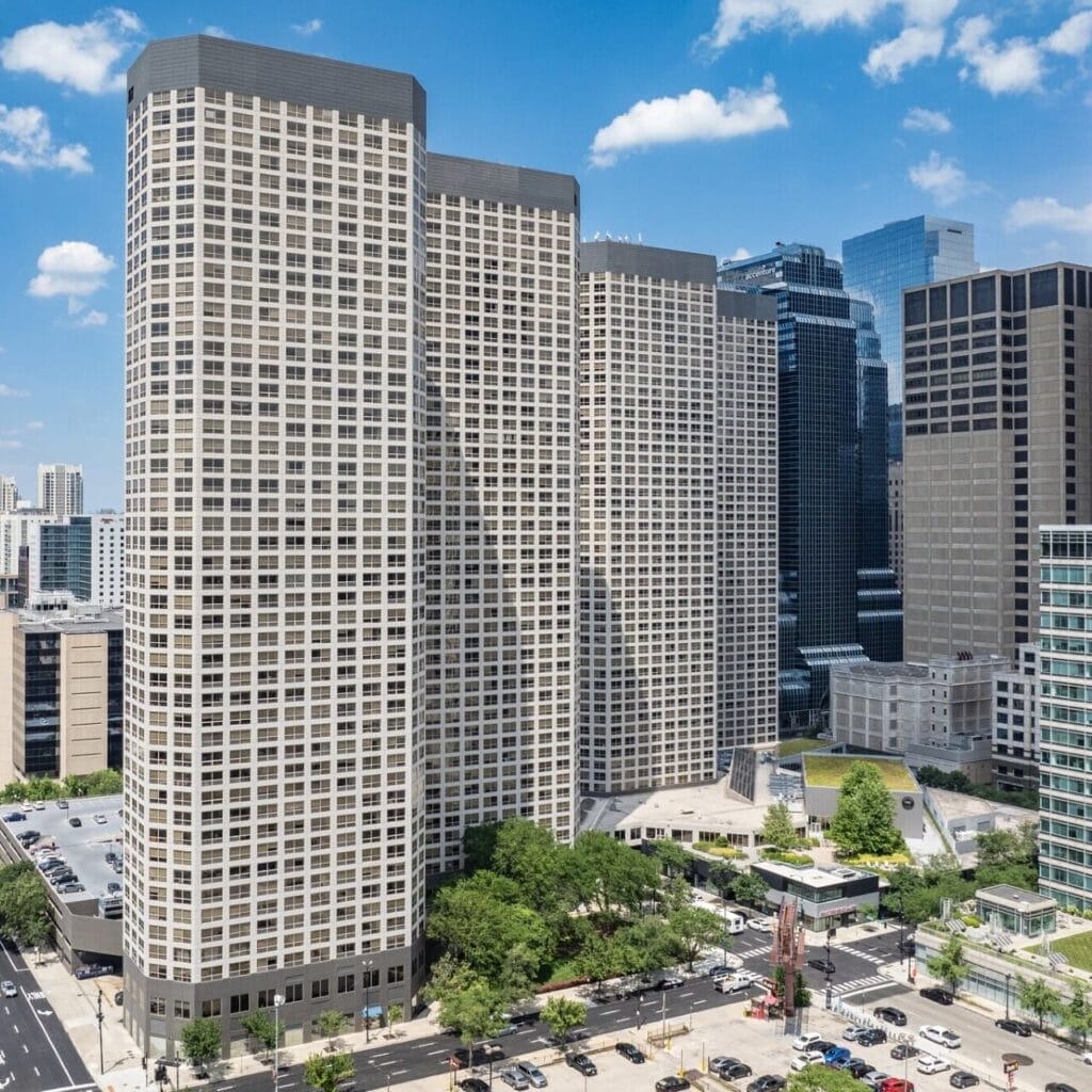 Downtown cityscape with modern high-rise buildings, clear blue sky, and surrounding streets and parked cars.