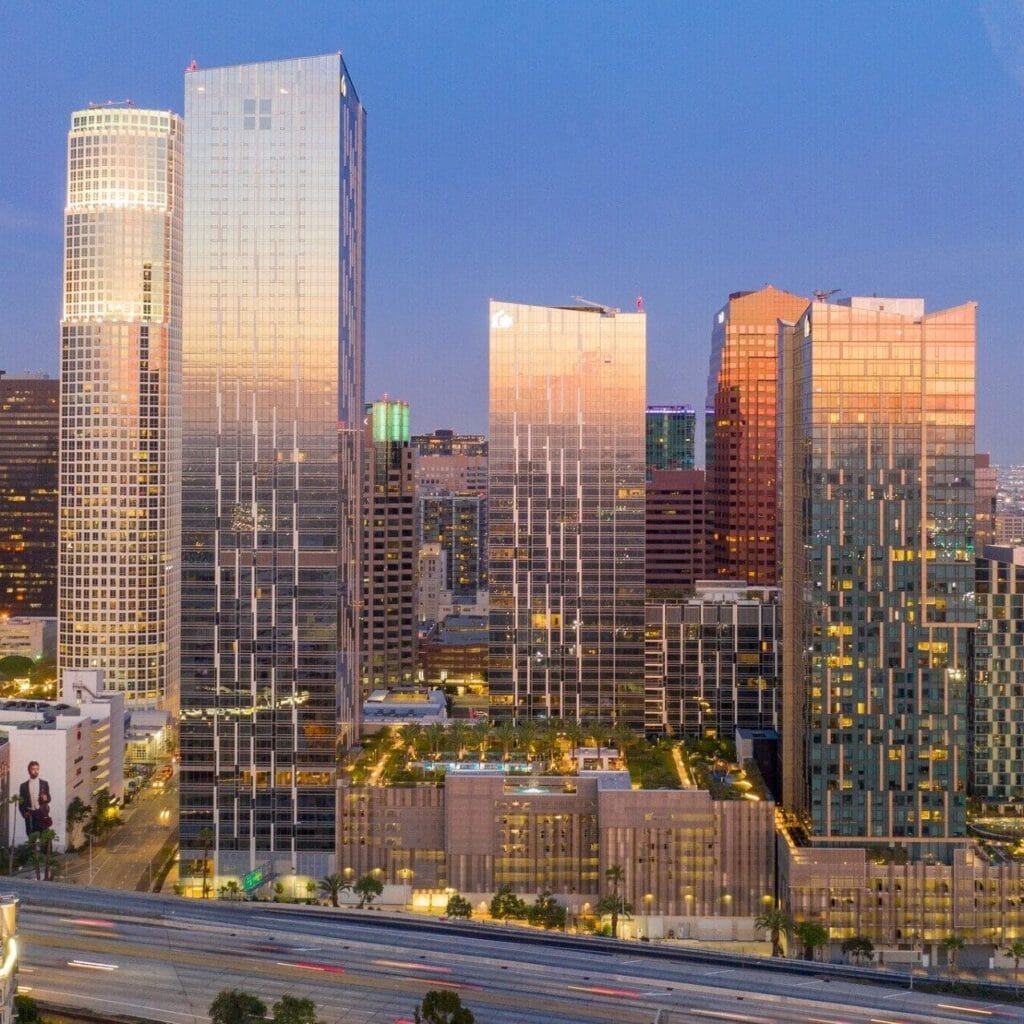 Downtown cityscape at dusk with tall glass skyscrapers reflecting light under a clear sky.